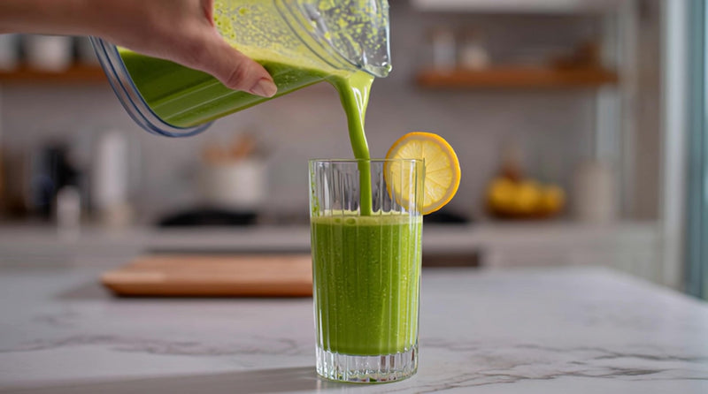 a person pouring a green smoothie into a glass with a slice of lemon on top set against a kitchen backdrop - Stock Video