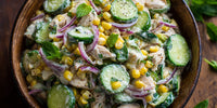 A Bowl Of Chicken Salad With Cucumbers And Corn Garnished With Mint Leaves Served In A Wooden Bowl On A Table — Stock Photo