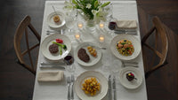 a dinner table setting for four with plates of food and wine glasses on a white tablecloth - Stock Video