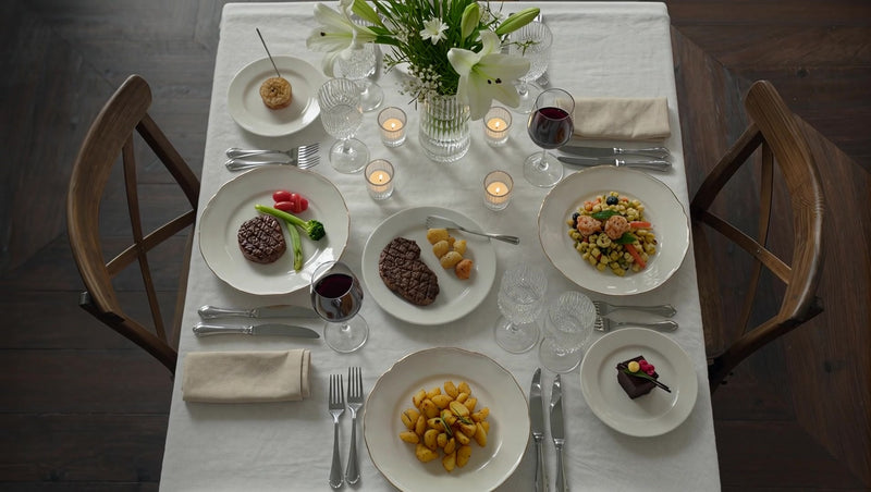 a dinner table setting for four with plates of food and wine glasses on a white tablecloth - Stock Video