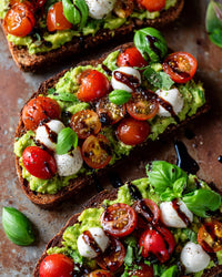 Avocado Toast With Tomatoes Mozzarella Balsamic Glaze And Basil Leaves On A Cutting Board — Stock Photo