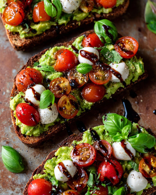 Avocado Toast With Tomatoes Mozzarella Balsamic Glaze And Basil Leaves On A Cutting Board — Stock Photo