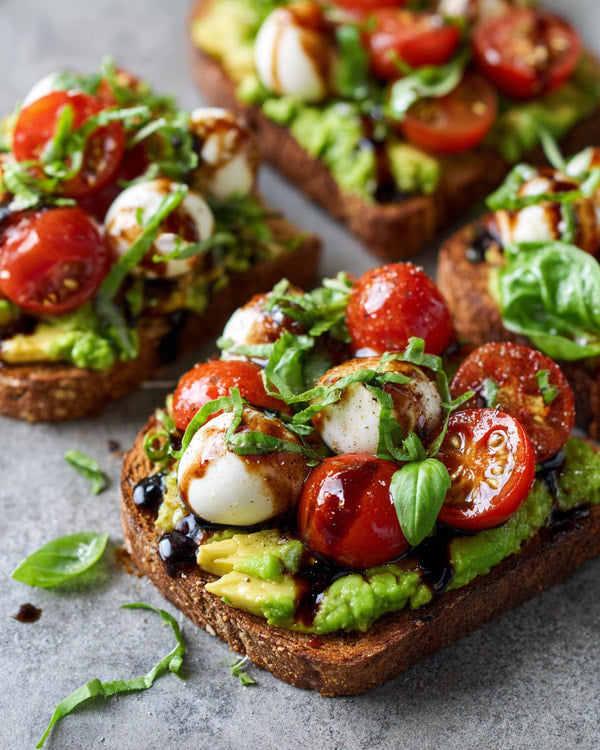 Photograph Of Three Slices Of Toasted Bread Each Topped With Avocado Tomato Mozzarella And Garnished With Fresh Basil Leaves — Stock Photo