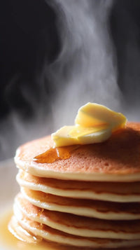 close up of a stack of pancakes with syrup on top steam rising from the hot dish set against a dark background - Stock Video