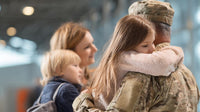 a soldier in uniform embraces a child and an adult surrounded by other people at an airport - Stock Video