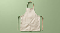 A Beige Apron With Tan Straps In A Studio Setting Placed On A Green Surface Against A Light Background — Stock Photo