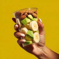A Person S Hand Holding A Clear Plastic Cup Filled With Assorted Fresh Fruits Including Bananas And Kiwi Slices Against A Yellow Background — Stock Photo