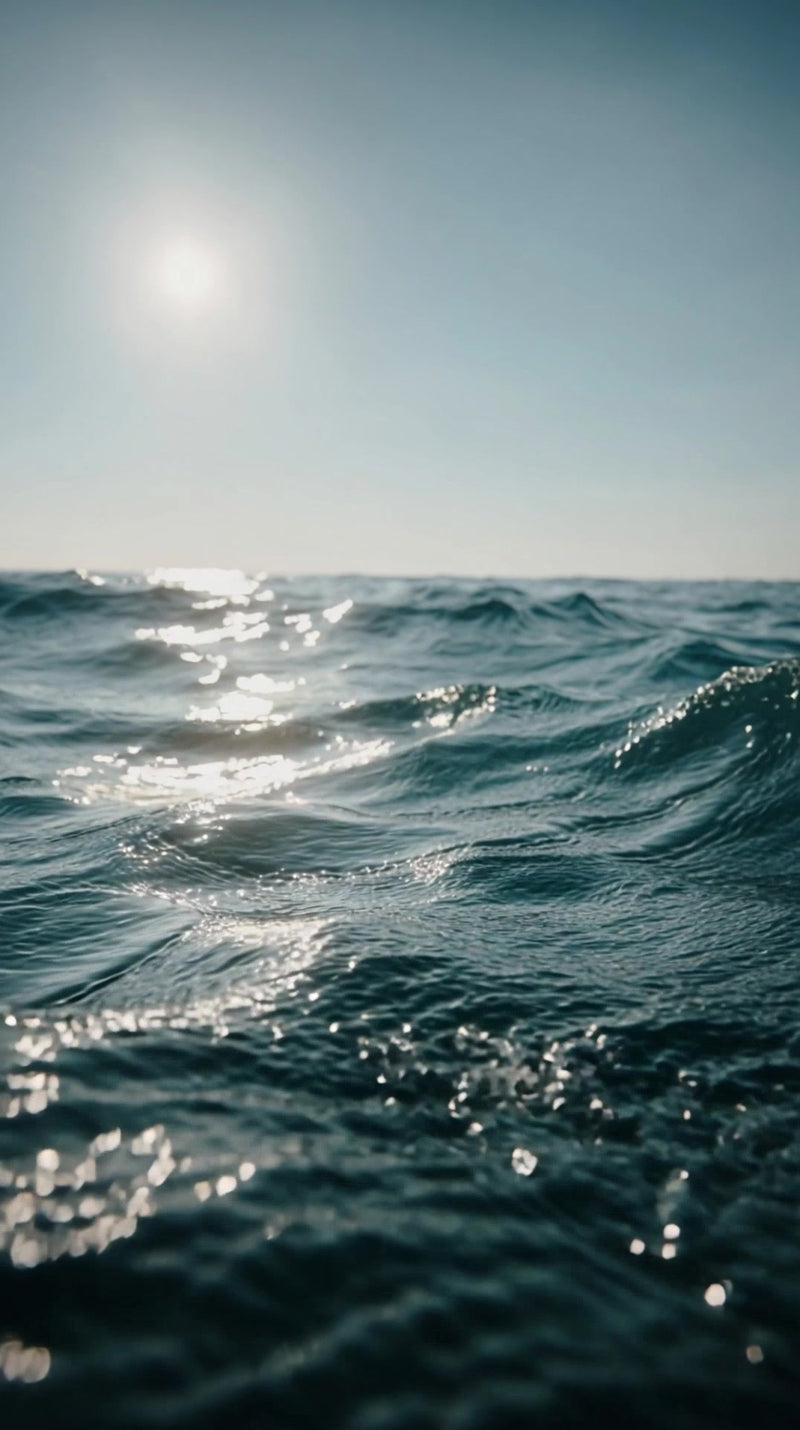 captures a serene ocean scene with the sun setting in the background and the sky transitioning from light to dark blue - Stock Video