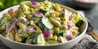 A Bowl Of Tasty Greek Salad With Visible Ingredients Such As Cucumbers Tomatoes And Chicken Shrimp Is Presented On A Table — Stock Photo