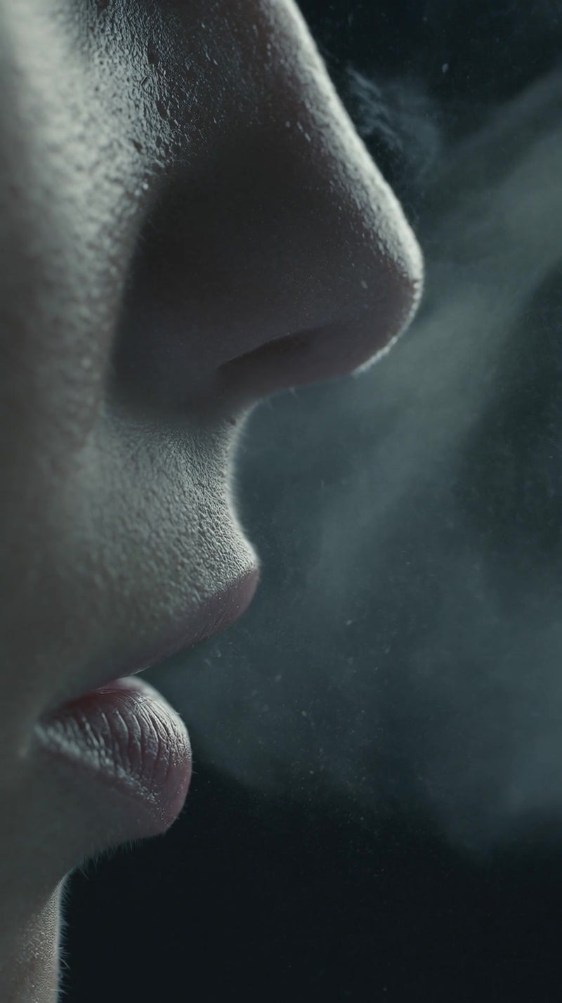 a close up of a person s face with smoke in the air captured from a side angle against a dark background - Stock Video