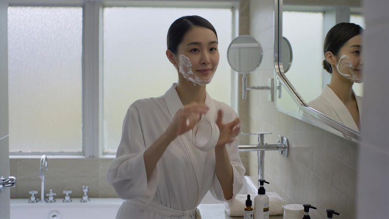 a woman in a bathrobe is standing at a bathroom sink applying makeup to her face - Stock Video