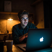 A Man Is Sitting At A Desk In A Dimly Lit Room Using A Laptop Computer — Stock Photo