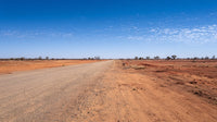 A Long Empty Dirt Road Stretches Across A Vast Expanse Of Flat Arid Landscape Under A Clear Blue Sky With Scattered Clouds — Stock Photo