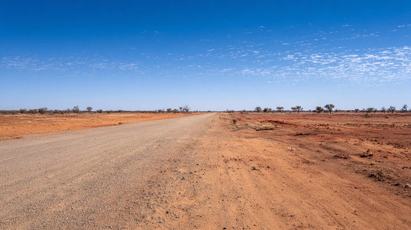 A Long Empty Dirt Road Stretches Across A Vast Expanse Of Flat Arid Landscape Under A Clear Blue Sky With Scattered Clouds — Stock Photo