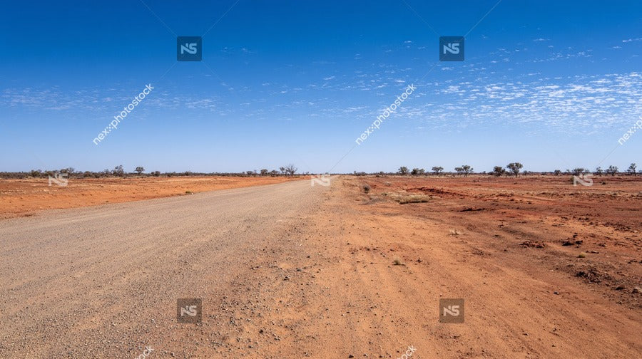 A Long Empty Dirt Road Stretches Across A Vast Expanse Of Flat Arid Landscape Under A Clear Blue Sky With Scattered Clouds — Stock Photo