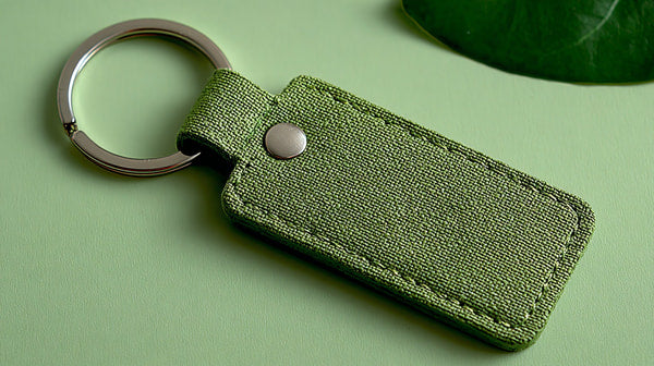 A Keychain With A Green Fabric Case And A Metal Button Placed On A Surface Against A Light Green Background — Stock Photo
