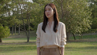 a woman wearing a tan blazer stands outdoors with trees and grass visible behind her - Stock Video