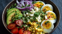 A Bowl Of Salad Containing Eggs Tomatoes And Avocado Garnished With Herbs And Spices Presented On A Dark Surface — Stock Photo