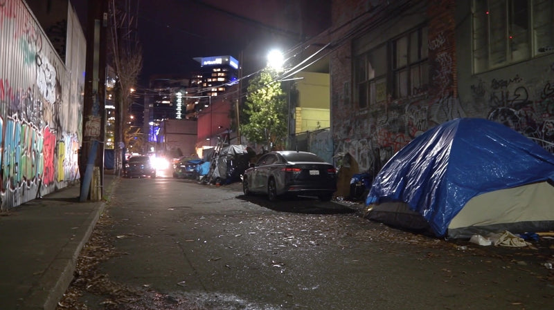an urban night scene an abandoned street with graffiti covered walls parked cars and a tent set up on the sidewalk - Stock Video