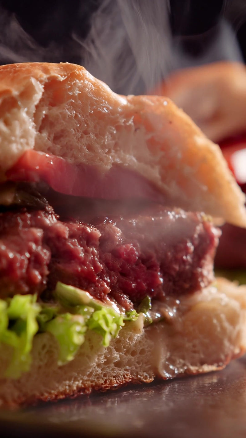 close up of a juicy burger on a bun with melted cheese and lettuce served in a restaurant setting - Stock Video