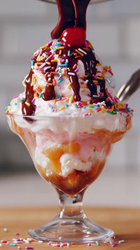 a delicious ice cream sundae with chocolate sauce and sprinkles served in a glass dish on a dining table - Stock Video
