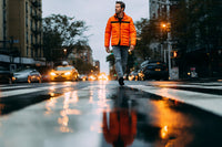A Man Is Walking Down A Wet City Street At Night Wearing An Orange Jacket — Stock Photo