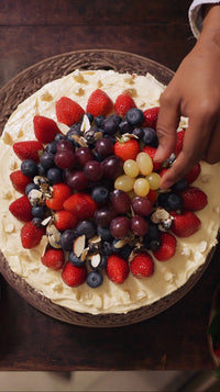 Shows A Person S Hand Reaching Towards A Cake That Is Decorated With An Assortment Of Fresh Fruits Including Strawberries Blueberries And Grapes — Stock Photo