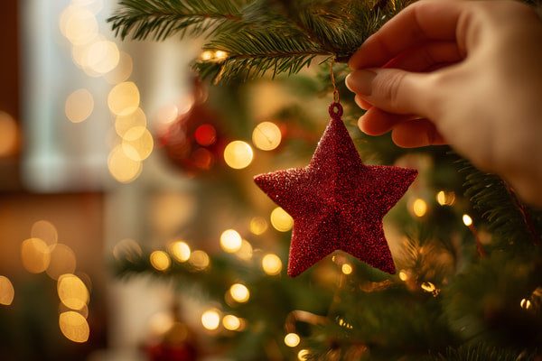 Hand Holding A Red Star Ornament On A Christmas Tree Decorated With Lights And Other Festive Decorations — Stock Photo