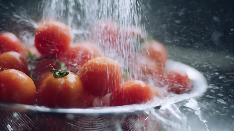 a bowl of cherry tomatoes is being rained upon with droplets of water splashing onto them - Stock Video