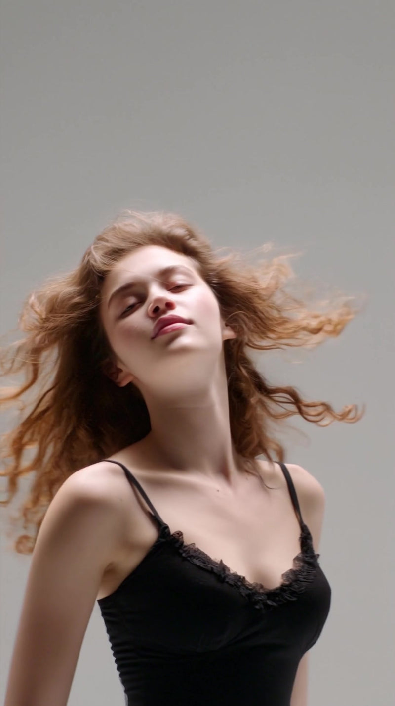 long haired woman in a black top captured from a side angle against a white background her hair caught mid motion by the wind - Stock Video