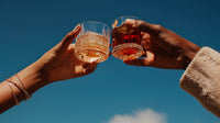 two individuals holding up glasses of whiskey in a celebratory toast against a blue sky background - Stock Video