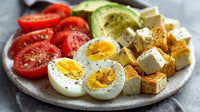 A Plate Of Assorted Foods Including Eggs Cheese Tomatoes And Avocado On A Table — Stock Photo