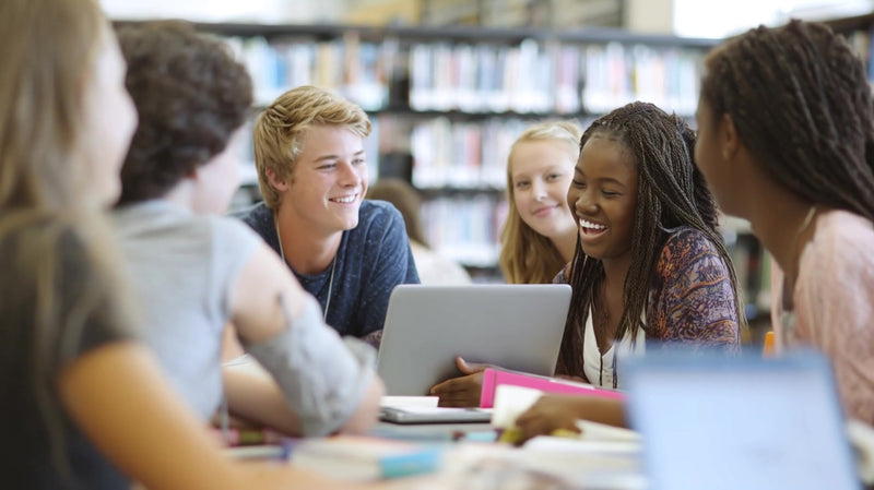 students gathered around a table in a library engaged in a discussion while using laptops - Stock Video