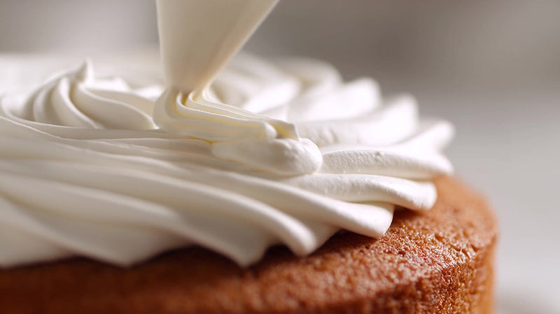 two images of a cake with white frosting and whipped cream being piped on top - Stock Video