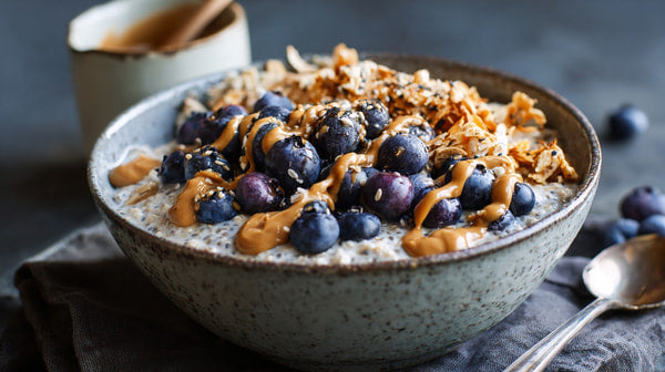 A Bowl Of Blueberry Oatmeal Topped With Nuts And Honey Served In A Grey Bowl On A Dark Surface — Stock Photo