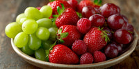 A Bowl Of Fresh Fruit Including Grapes Strawberries And Plums Displayed On A Table — Stock Photo