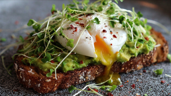 A Slice Of Toasted Bread Topped With A Fried Egg And Avocado Garnished With Microgreens And Red Pepper Flakes — Stock Photo