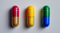 Four Pills Displayed On A White Surface With Each Pill Exhibiting A Different Color Red Green Yellow And Blue — Stock Photo