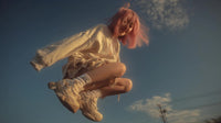 a young woman with pink hair is captured mid jump suspended in the air against a clear blue sky background - Stock Video