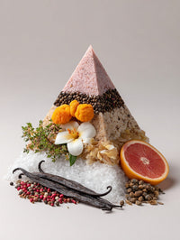A Pyramid Shaped Display Of Various Food Items Including A Slice Of Orange And Spices Set Against A Backdrop Of White Sand — Stock Photo