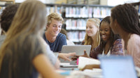teenagers gathered around a table in a library engaged in conversation and using laptops - Stock Video