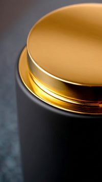 A Close Up Of A Gold Lid On A Black Canister With A Focus On The Contrast Between The Two Colors And Materials — Stock Photo