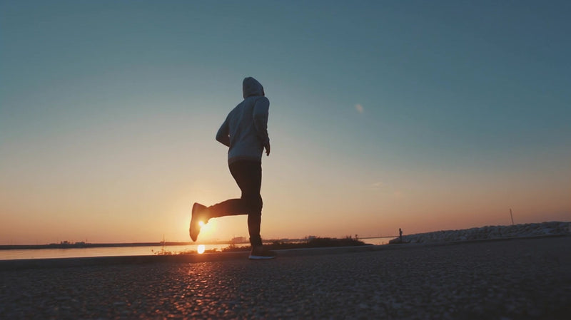 a person jogging during sunset captured in silhouette against a backdrop of a clear sky and calm sea - Stock Video