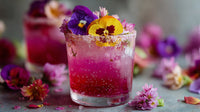 A Glass Of Purple Flower Garnished Drink With A Colorful Floral Arrangement On A Table — Stock Photo